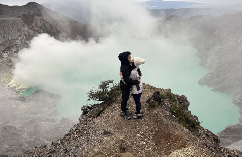 A guest on the Ijen crater rim with sulfur smoke over the lake